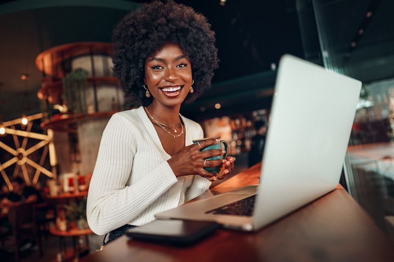Person holding a coffee mug while using laptop at a coffee shop.