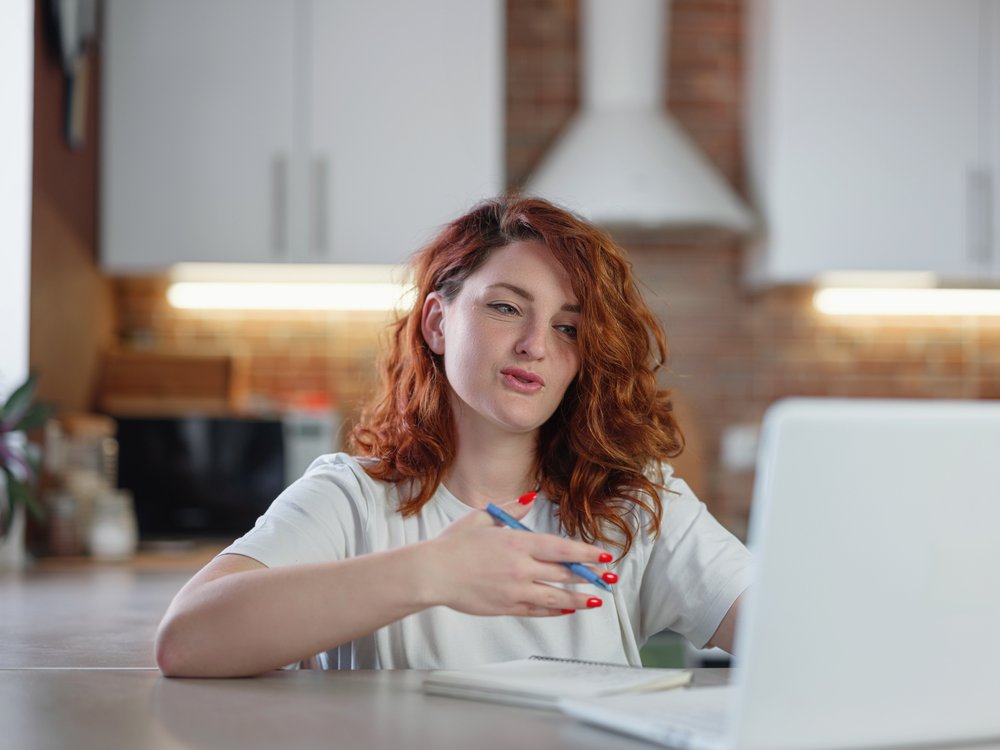 Student speaking while using laptop at kitchen table.