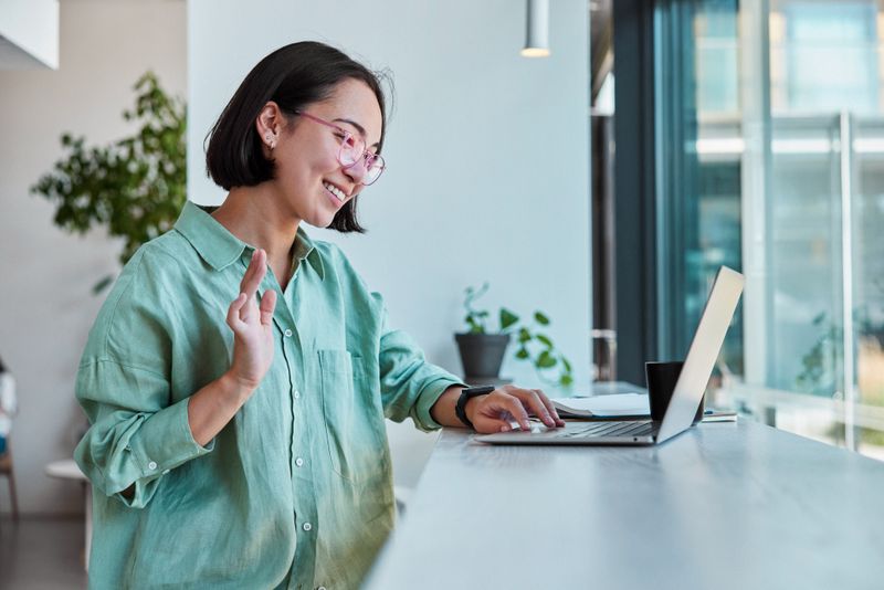 Student waving at laptop screen during online class