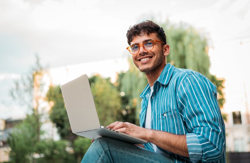 Student sitting outside holding laptop.