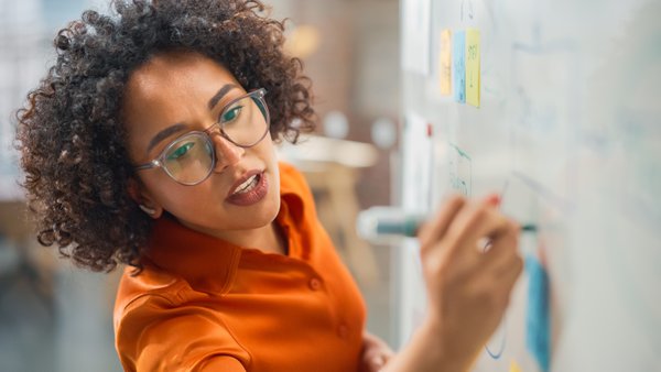 Individual writing on a whiteboard in an orange shirt.
