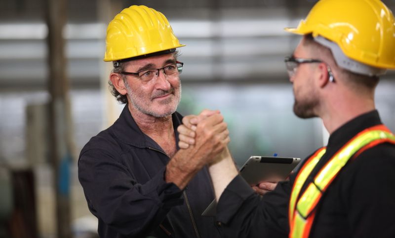Two safety professionals shaking hands in an industrial workplace.