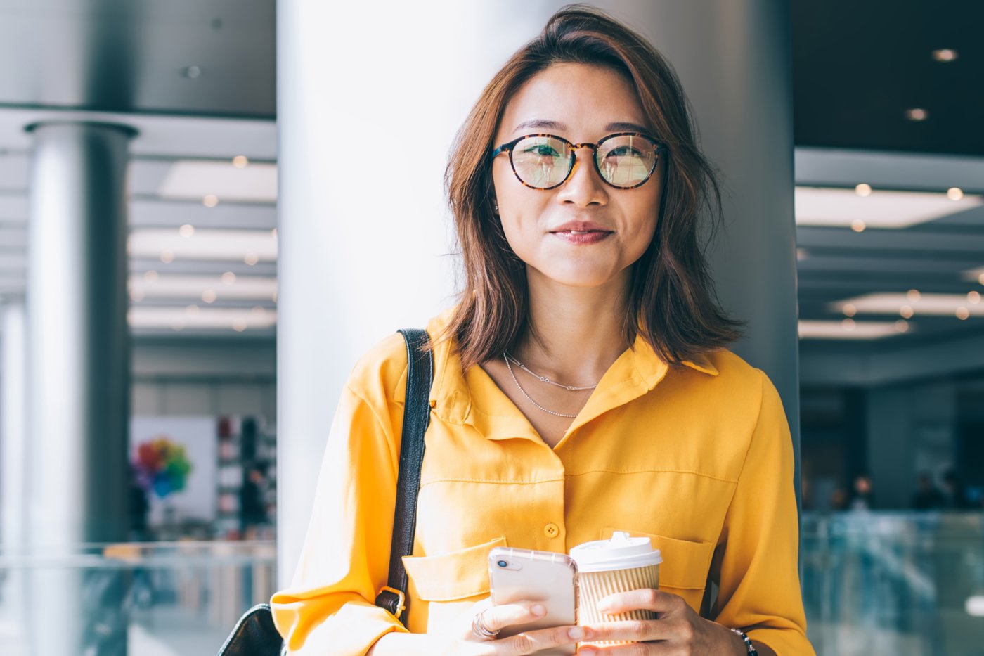 Student holding phone and coffee mug in indoor space