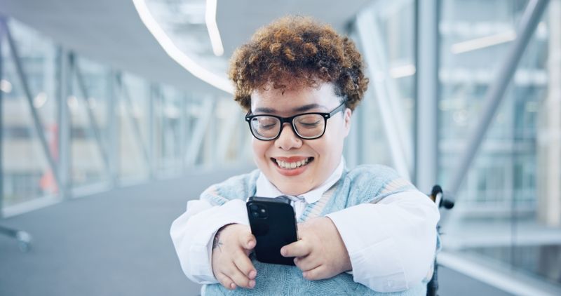 Student using mobile device in modern hallway.