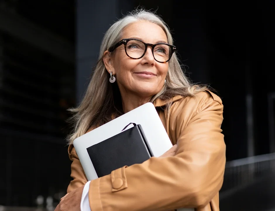 Person with glasses holds a notebook and laptop computer.
