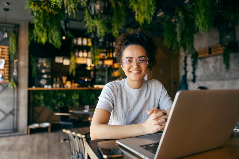Student smiling while working on a laptop in downtown cafe